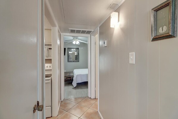 A narrow hallway with a ceiling fan, a bed in the background, and a laundry area to the left.