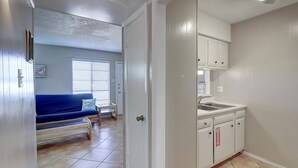 A compact room with a kitchenette, a bed, and a window with blinds. - This is the perfect cozy island bungalow for a weekend of fishing or just hangin (Port Aransas)