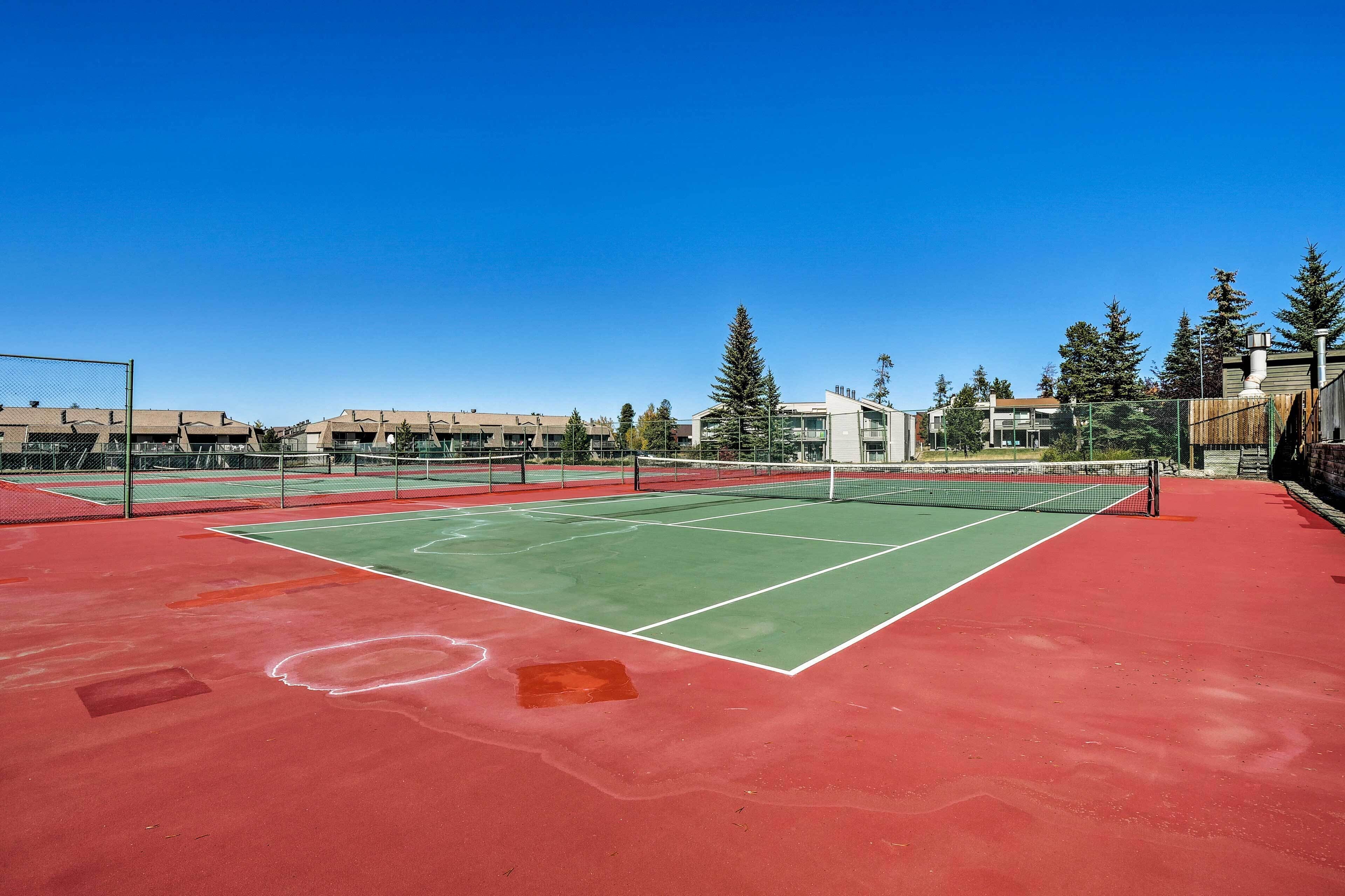 A tennis court with a net, surrounded by buildings and trees.