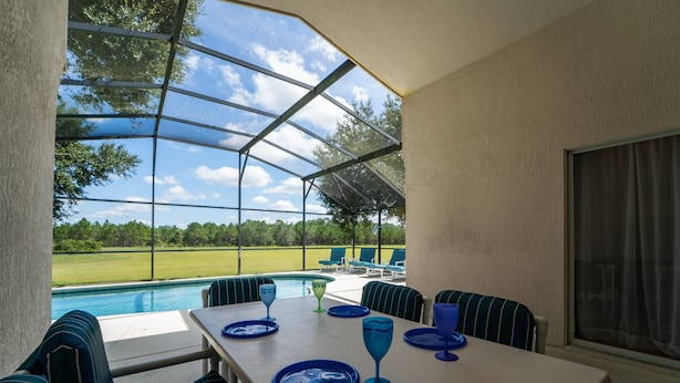Un patio techado con vista a la piscina, mobiliario exterior y una mesa lista para comer.