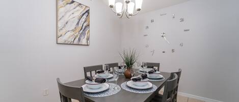 A dining room with a dark wooden table, white plates, and a chandelier.
