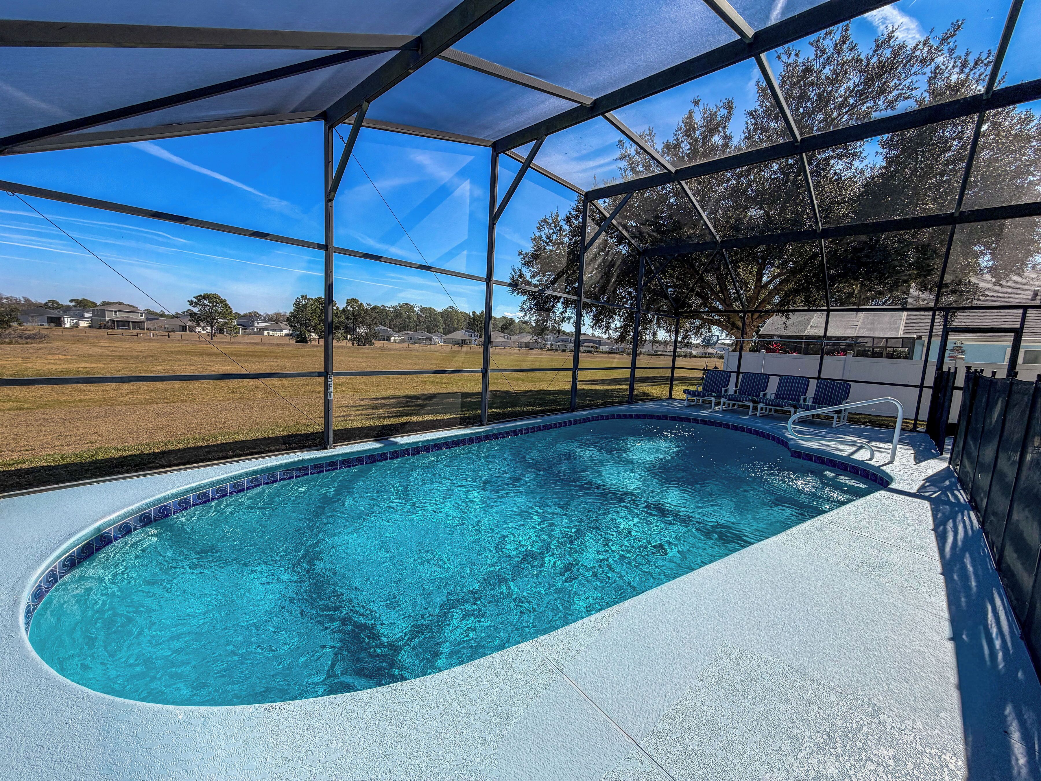 A swimming pool with a clear blue water, surrounded by a covered area with chairs and a view of a residential area.