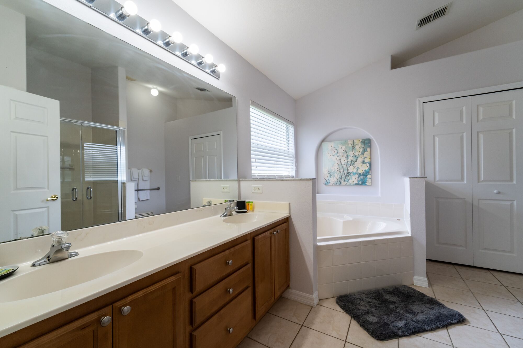 A bathroom with a large mirror, a sink, a bathtub, and a small rug.