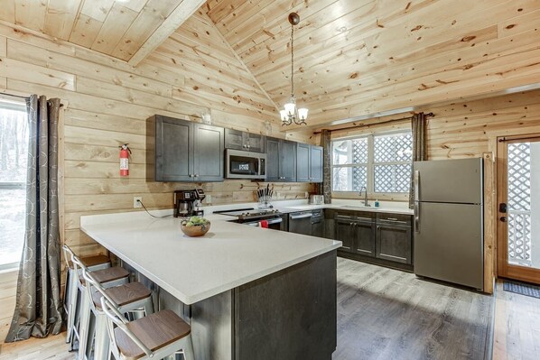 Una cocina moderna con paredes de madera, una isla central, taburetes de bar, electrodomésticos de acero inoxidable y una araña.