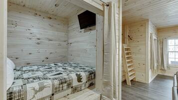 Eine Holzhütte mit einem Bett, einem Fernseher und einem Fenster.