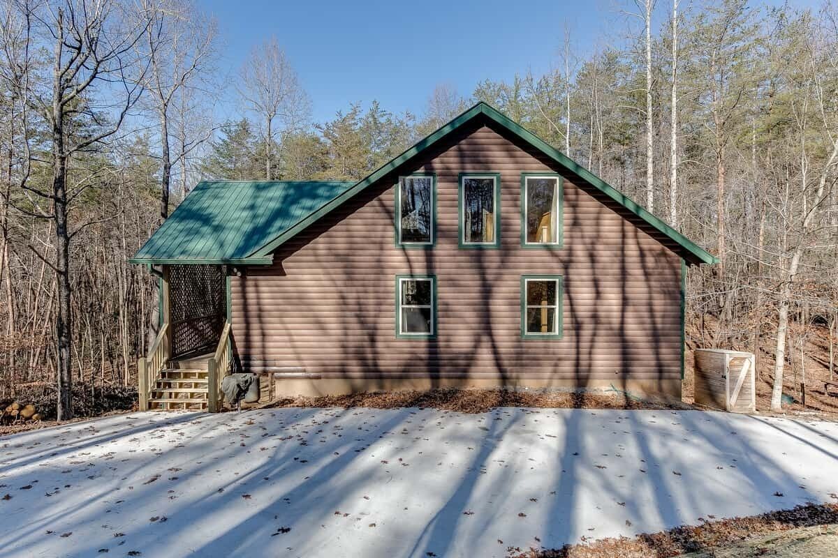 Una cabaña de madera con techo verde, rodeada de árboles y un suelo cubierto de nieve.