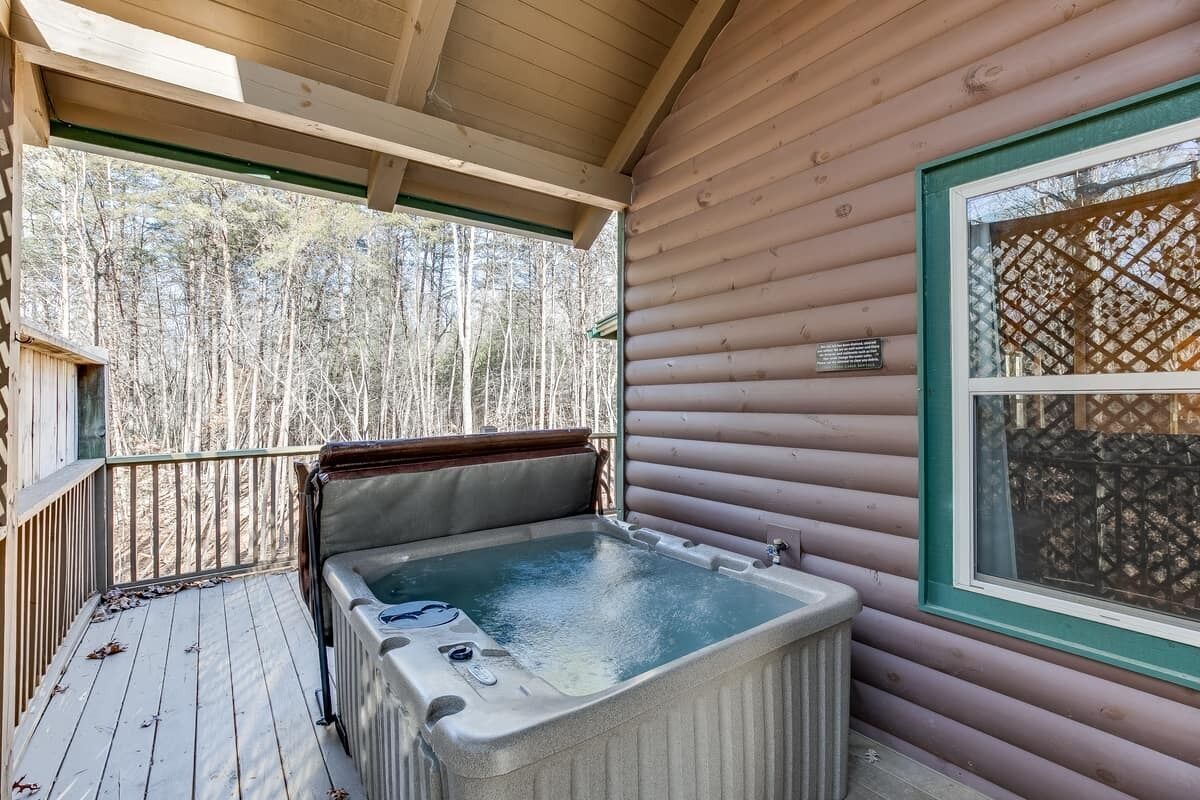 Una cabaña de madera con jacuzzi en una terraza, rodeada de árboles.