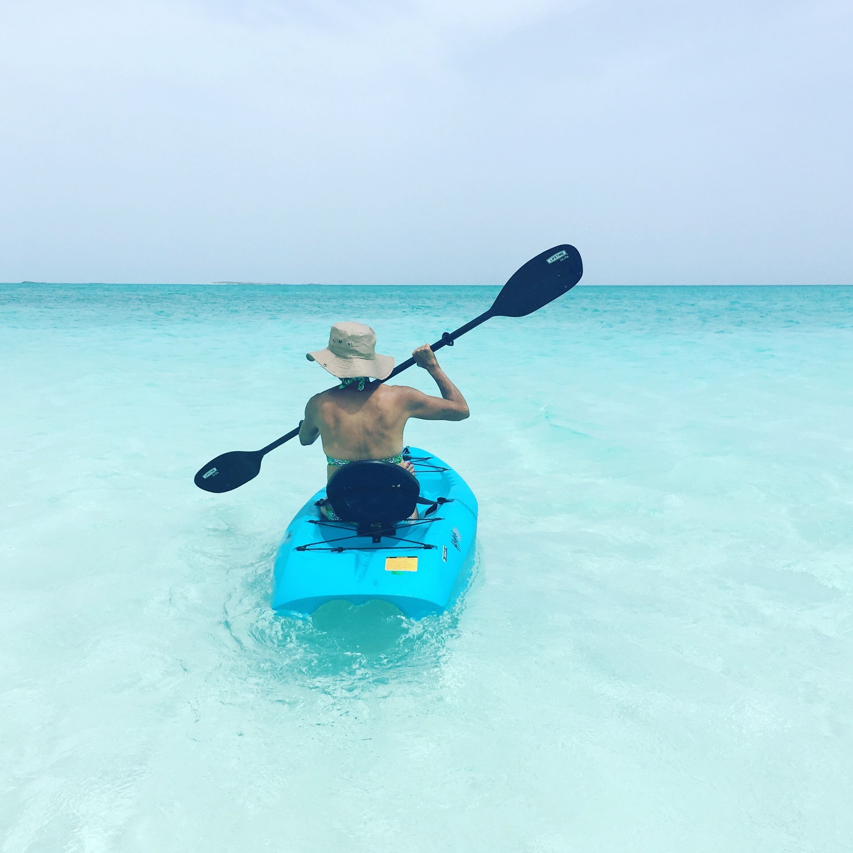 A person kayaking on a clear turquoise sea.