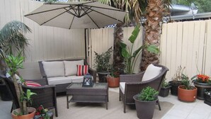 Eine Terrasse im Freien mit Korbmöbeln, einem Glastisch und verschiedenen topfgepflanzten Pflanzen.