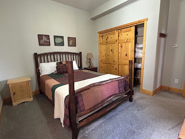 Une chambre à coucher avec un lit en bois, une table de chevet, une armoire et trois tableaux encadrés accrochés au mur.