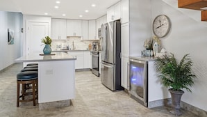 Una cocina moderna con armarios blancos, electrodomésticos de acero inoxidable, una isla central con taburetes y una planta en maceta.