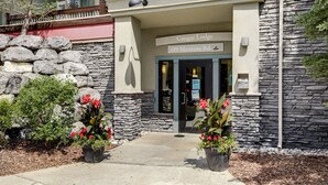 L’extérieur du Cougar Lodge, situé au 109, Montana Rd., se distingue par sa façade en pierre, son entrée accueillante et ses plantes en pot ornées de fleurs rouges.