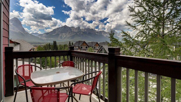 Un balcon avec une table et des chaises, donnant sur un paysage montagneux avec des maisons en arrière-plan.