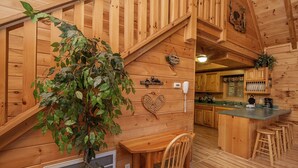 Interior de una cabaña de madera con una escalera, una barra y una cocina.