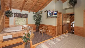 Interior de una cabaña de madera con jacuzzi, cama, televisor y escalera.
