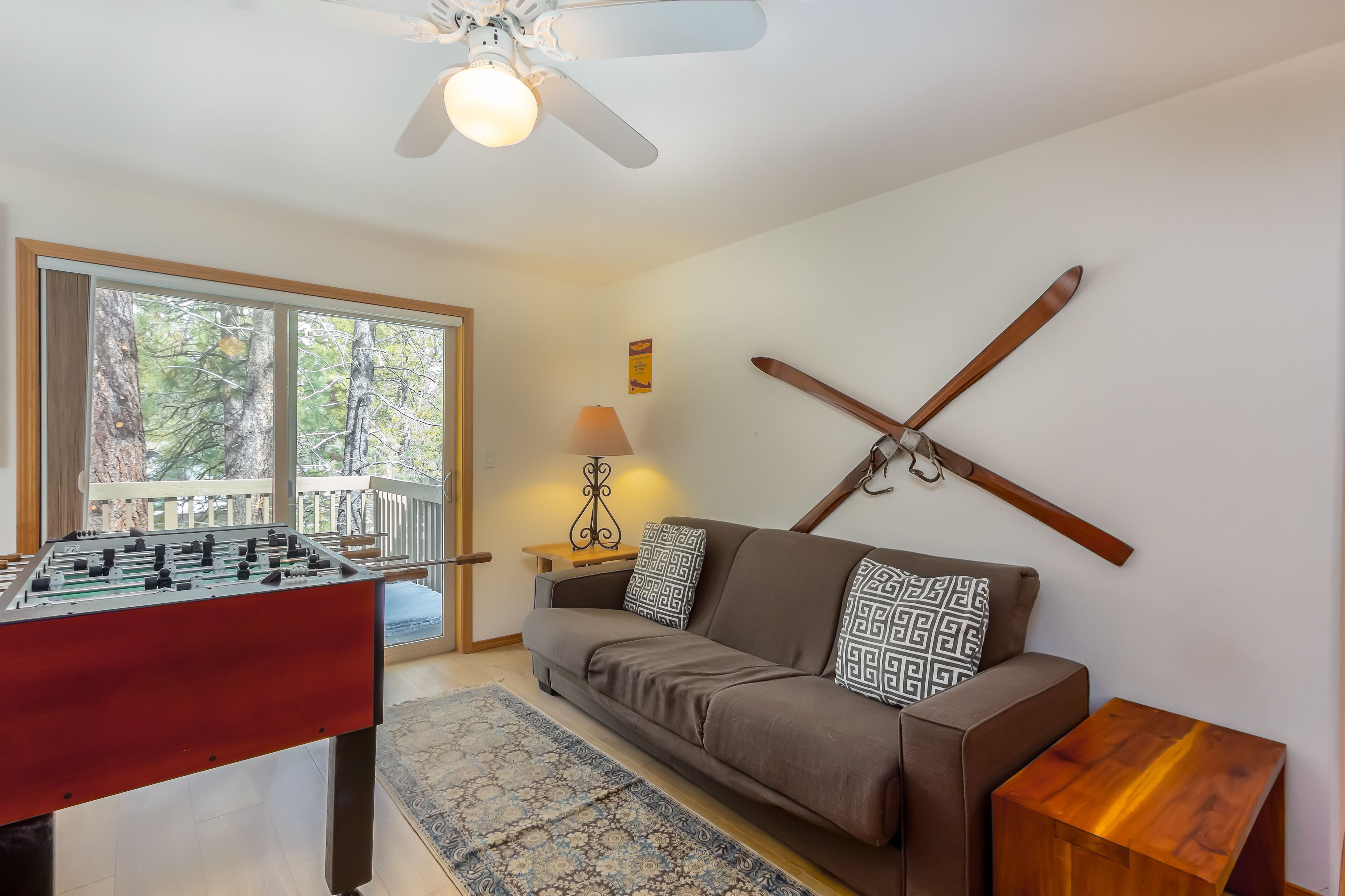 A cozy living room with a foosball table, a sofa, a coffee table, and a large window with a view of trees.