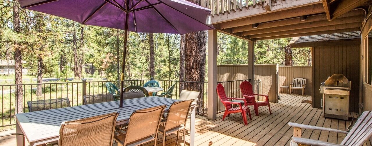 Une terrasse en bois avec une table et des chaises, un barbecue et un espace abrité avec un parasol violet.