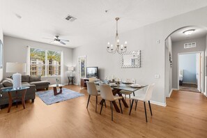 A modern living room with a dining area, a chandelier, and a large window. - Premium 3BR condo Resort Perks near Epic Universe (Orlando)