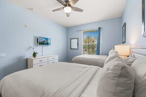 A bedroom with two beds, a ceiling fan, a window with blinds, a bedside table with a lamp, and a wall-mounted TV. - Premium 3BR condo Resort Perks near Epic Universe (Orlando)