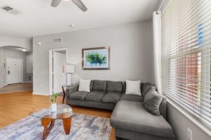 A modern living room with a sectional sofa, a glass coffee table, and a painting on the wall. - Premium 3BR condo Resort Perks near Epic Universe (Orlando)