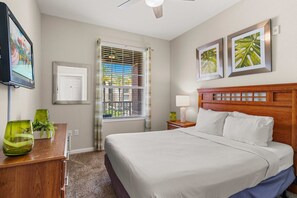 A hotel room with a bed, a desk with a lamp, a television, and a window with blinds. - Premium 3BR condo Resort Perks near Epic Universe (Orlando)
