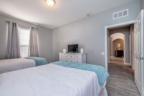 Ein Schlafzimmer mit zwei Betten, einem Fernseher auf einer Kommode und einem Flur, der in einen weiteren Raum führt.