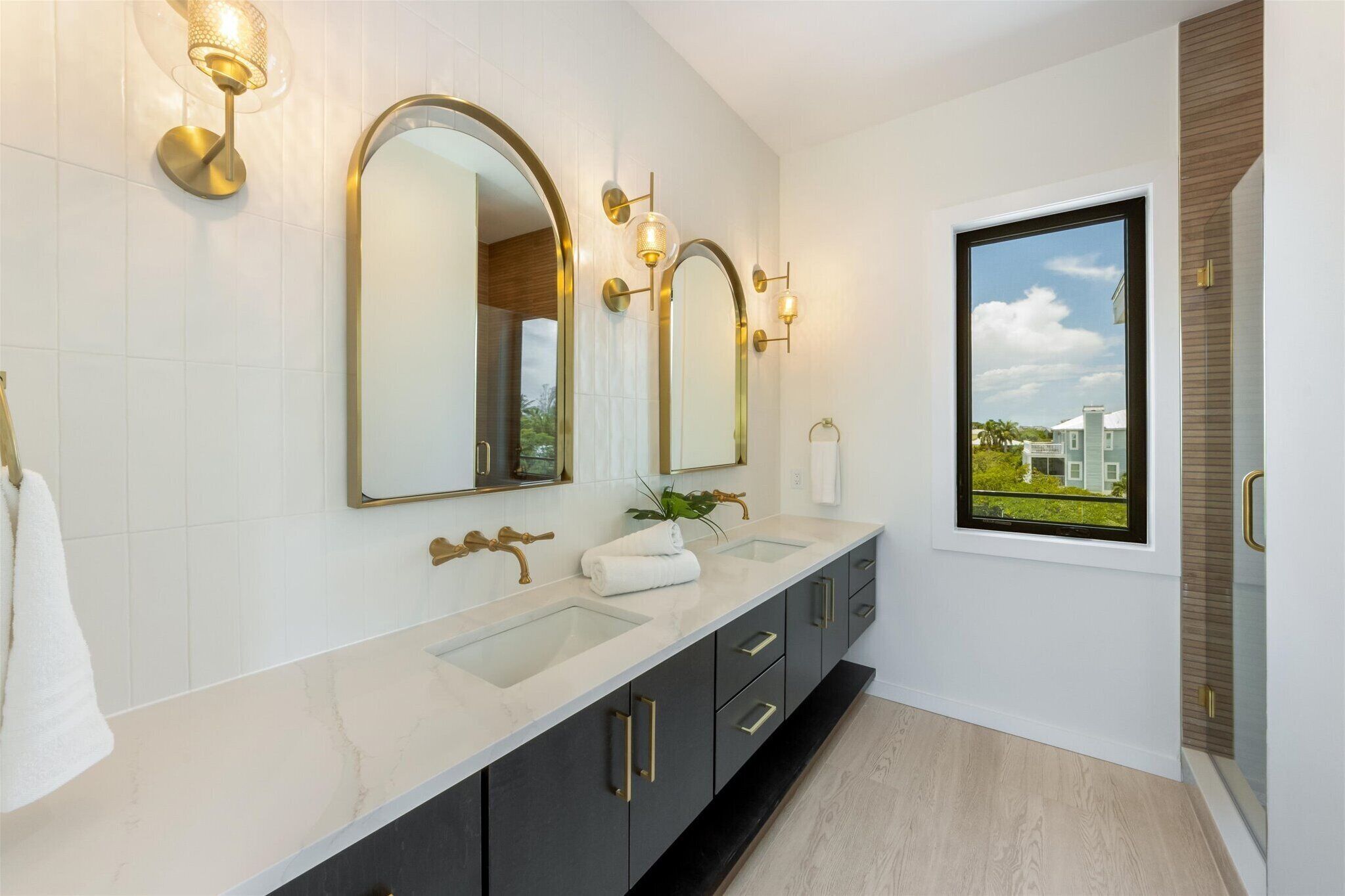Une salle de bain moderne avec deux vasques, un grand miroir, des appliques murales et une fenêtre donnant sur un beau paysage.