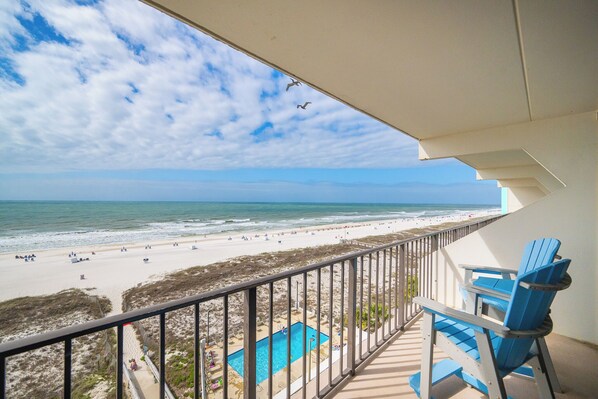 A balcony with a view of a beach, a pool, and a chair.