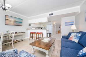 A modern living room with a blue sofa, wooden coffee table, and a dining area with a wooden table and chairs.