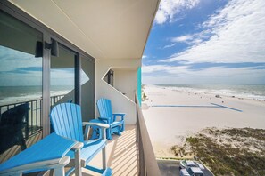A balcony with blue chairs and a view of a beach.