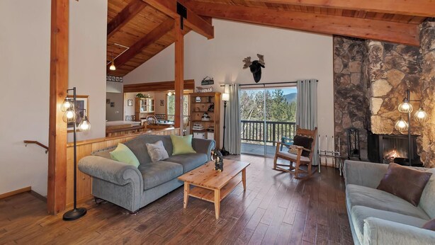 Ein gemütliches Wohnzimmer mit Kamin aus Stein, Holzbalken und einem Essbereich, der durch eine Glastür erblickt werden kann.