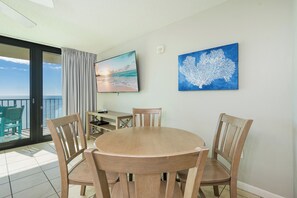 Un coin repas avec une table ronde et quatre chaises, un téléviseur à écran plat fixé au mur et un tableau représentant un récif corallien.