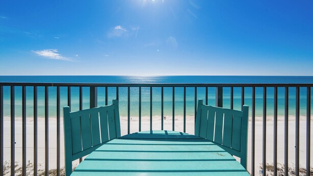 Une vue depuis un balcon donnant sur une plage, avec un ciel dégagé et un soleil éclatant.