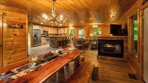 A wooden cabin interior with a dining area, kitchen, and fireplace. - Budget-Friendly | Theater Room, Hot Tub, Gameroom (Gatlinburg)