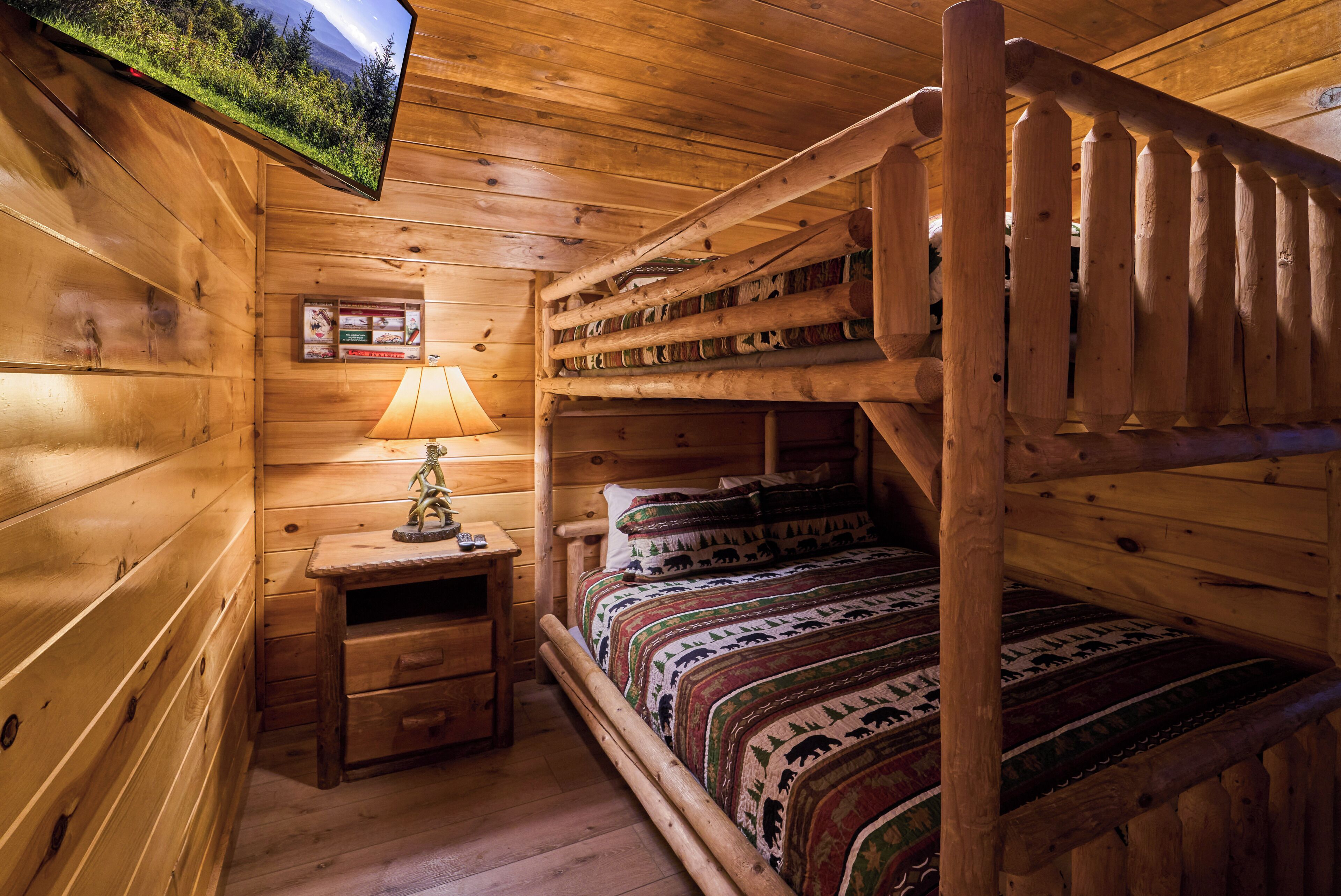A wooden cabin room with a bunk bed, a nightstand with a lamp, and a mounted television.