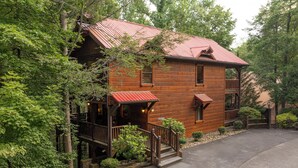 A wooden cabin with a red roof, a porch, and a staircase leading to the entrance. - Budget-Friendly | Theater Room, Hot Tub, Gameroom (Gatlinburg)