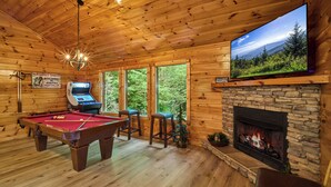 A wooden cabin interior with a pool table, a fireplace, and a television mounted on the wall. - Budget-Friendly | Theater Room, Hot Tub, Gameroom (Gatlinburg)