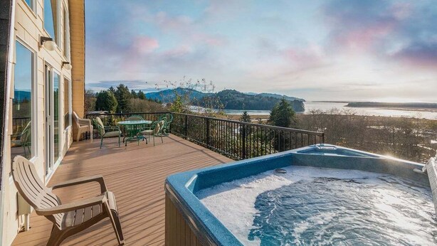 Un bain à remous sur une terrasse en bois, avec vue sur une plage et des montagnes.