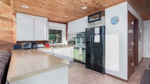 Une cuisine moderne avec un plafond en bois, des armoires blanches, un réfrigérateur noir et une grande fenêtre.