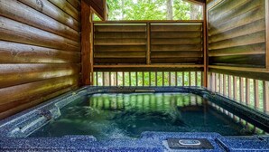 A hot tub in a wooden cabin with a view of trees through a window.