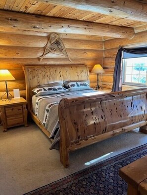 Un dormitorio de cabaña de madera con una cama, dos mesitas de noche y una ventana.