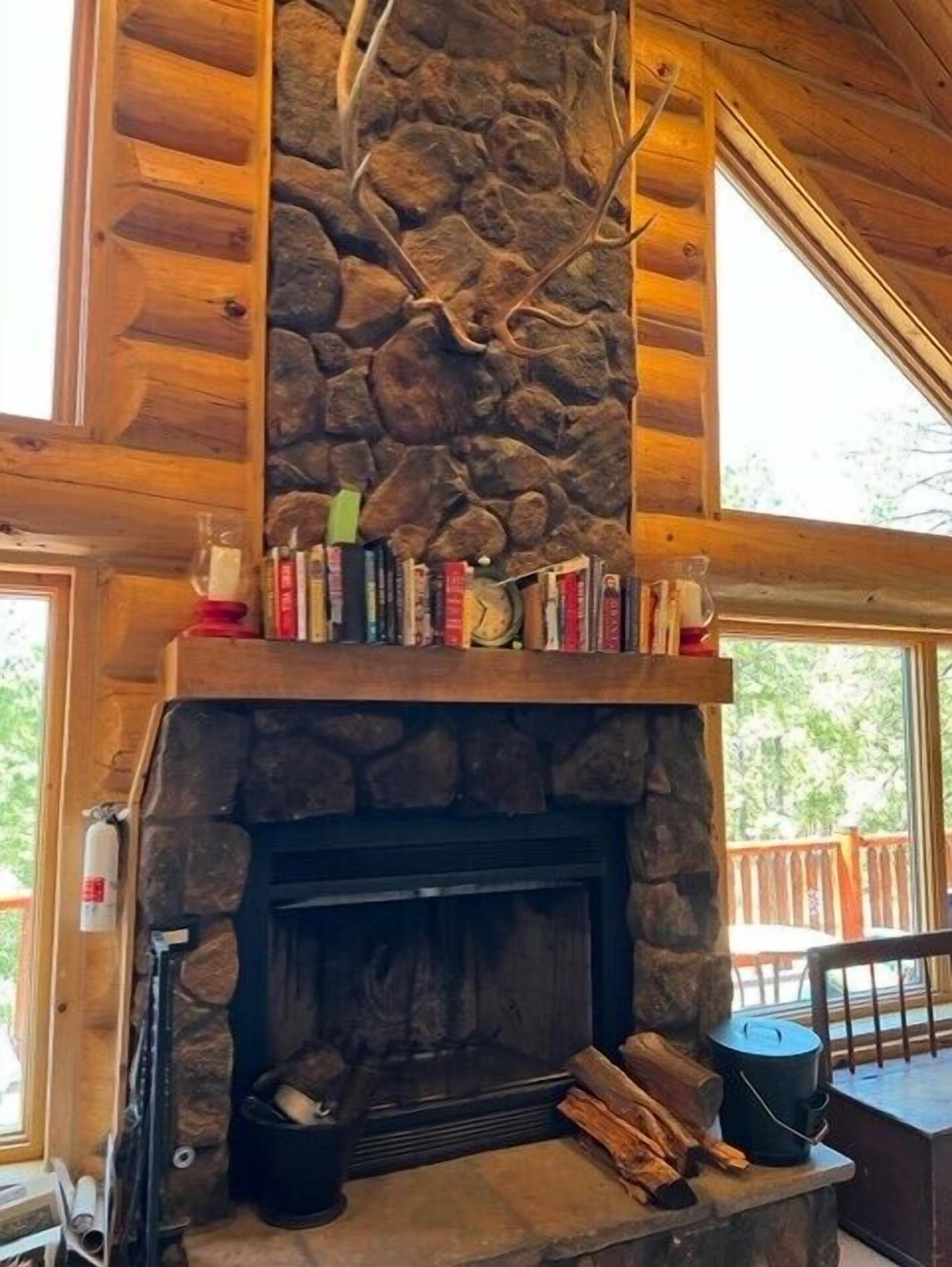 A stone fireplace with a wooden mantel, books, and logs.