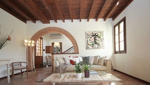 Una sala de estar acogedora con techo de madera, un arco de ladrillo, un sofá, una mesa de centro con plantas y un cuadro en la pared.