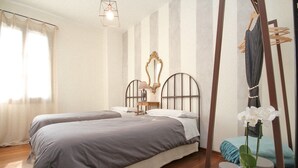 Un dormitorio con dos camas, piso de madera, una silla colgante, una lámpara y una planta en maceta.