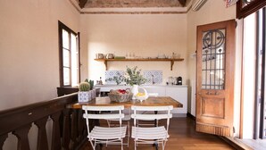 Una cocina acogedora con una mesa de madera, dos sillas blancas y diversos utensilios de cocina en las estanterías.