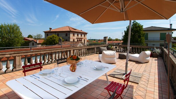 Una terraza con mesa lista para comer, asientos al aire libre y un toldo grande que proporciona sombra.