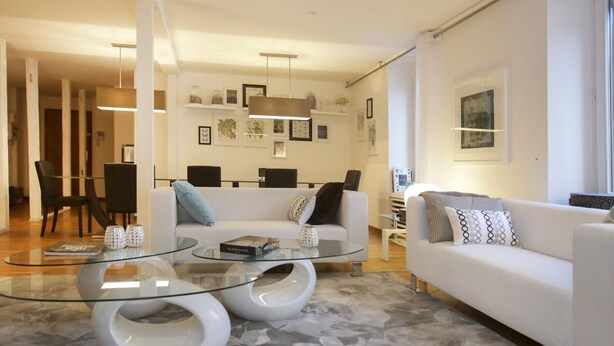 Una sala de estar moderna con un sofá blanco, una mesa de centro de vidrio y un comedor al fondo.