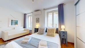 Un dormitorio moderno con una cama, dos mesitas de noche con lámparas, un sofá y una ventana con cortinas.