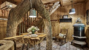 A rustic interior with a wooden dining table surrounded by tree trunks, a rocking chair, and a vintage stove. - ER69 - Rachel's Tree House - Great location. Close to all the action! (Pigeon Forge)