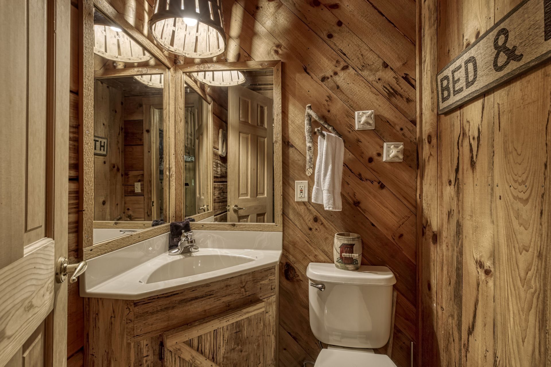 A rustic bathroom with a wooden interior, a sink, a toilet, and a mirror.